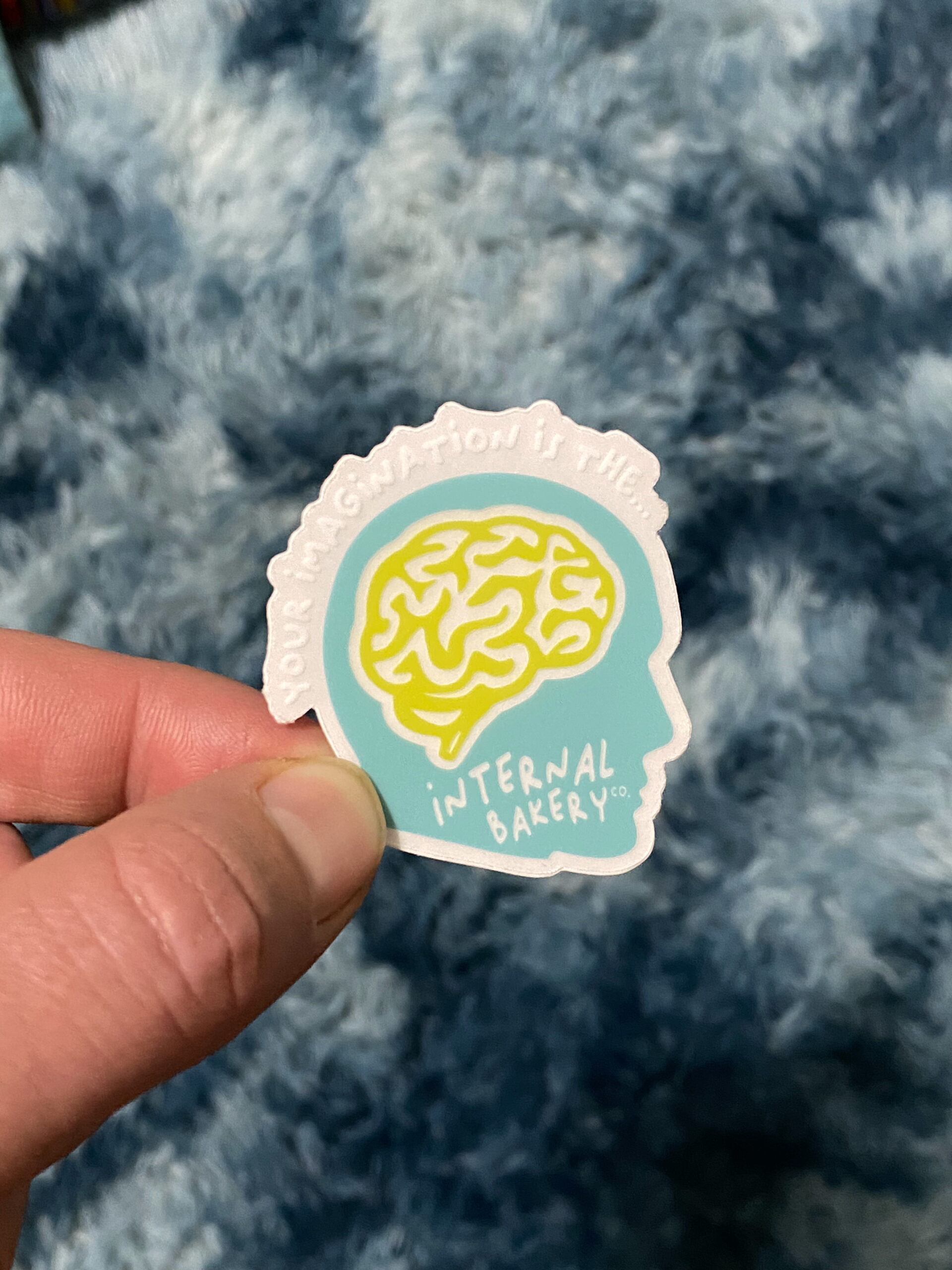 “Your Imagination Is The…” Clear Head Sticker (1.96″ × 2″) A peek inside the bakery of your mind 🍞💭 This trippy lil’ sticker puts your imagination on display — literally. The clear design lets your surroundings show through the brain and face, blending your world into the art itself. It’s a blue head, a chartreuse brain, and a reminder that the wildest ideas live upstairs. Stick it on your laptop, water bottle, or mirror — anywhere you wanna remember that your imagination is the Internal Bakery.