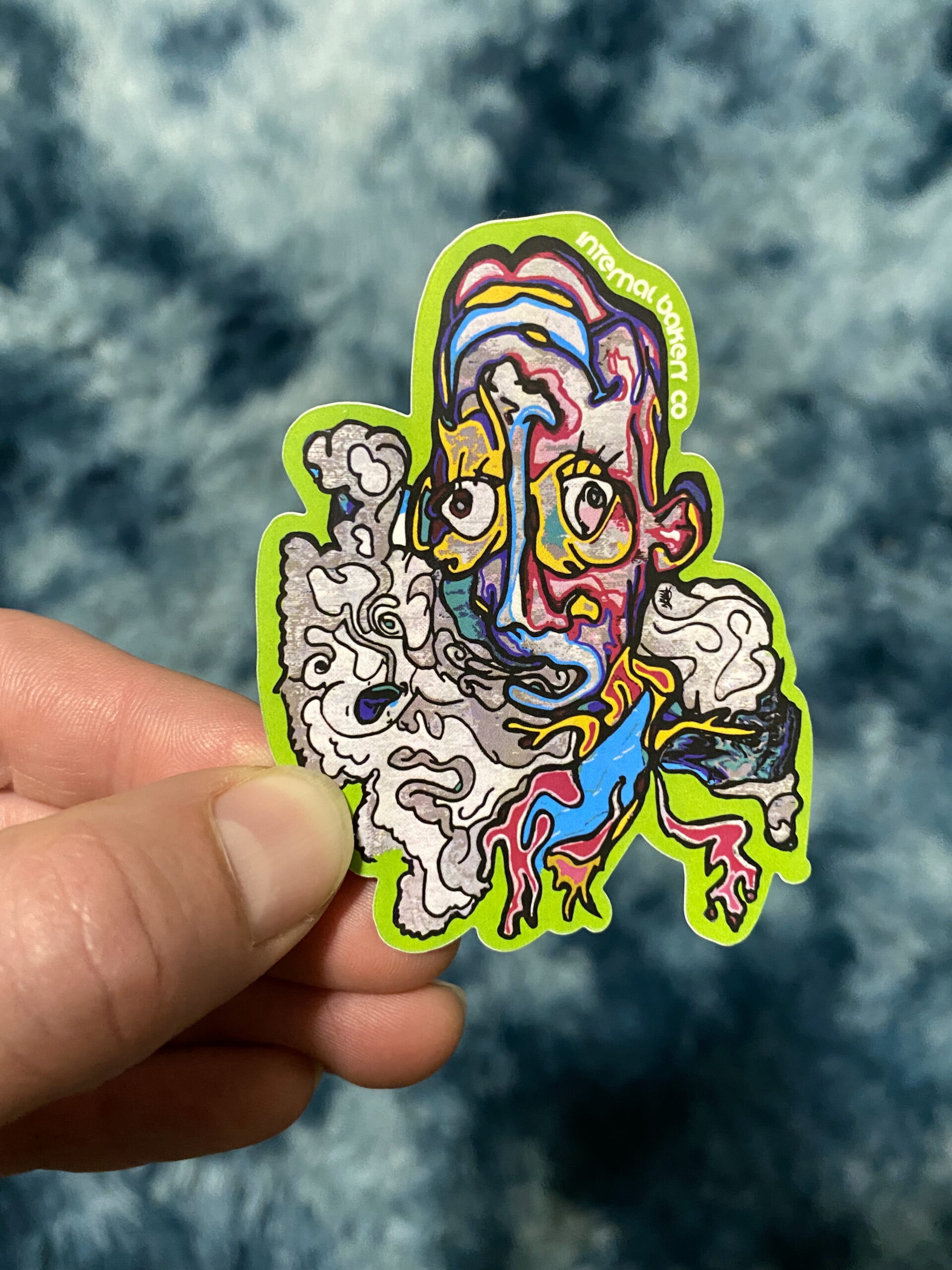 HAZY 2FACE STICKER — 3″ Step into the smoke with Hazy 2Face, a mind-bending character straight from the Internal Bakery imagination. Look at him one way and he’s kickin’ back, blowing out a hazy puff — flip him upside down and suddenly you’re face-to-face with a happy clown from another dimension. Part of the fan-favorite 2Face Series, this hand-drawn design is all about duality, perception, and seeing how imagination can flip the world around you. Perfect for laptops, water bottles, and anywhere you want to remind yourself that there’s always another side to the story. — Hand-drawn by Zach Ray in Colorado Springs, CO — 3″ durable vinyl sticker — Twist it. Flip it. Smoke it out.
