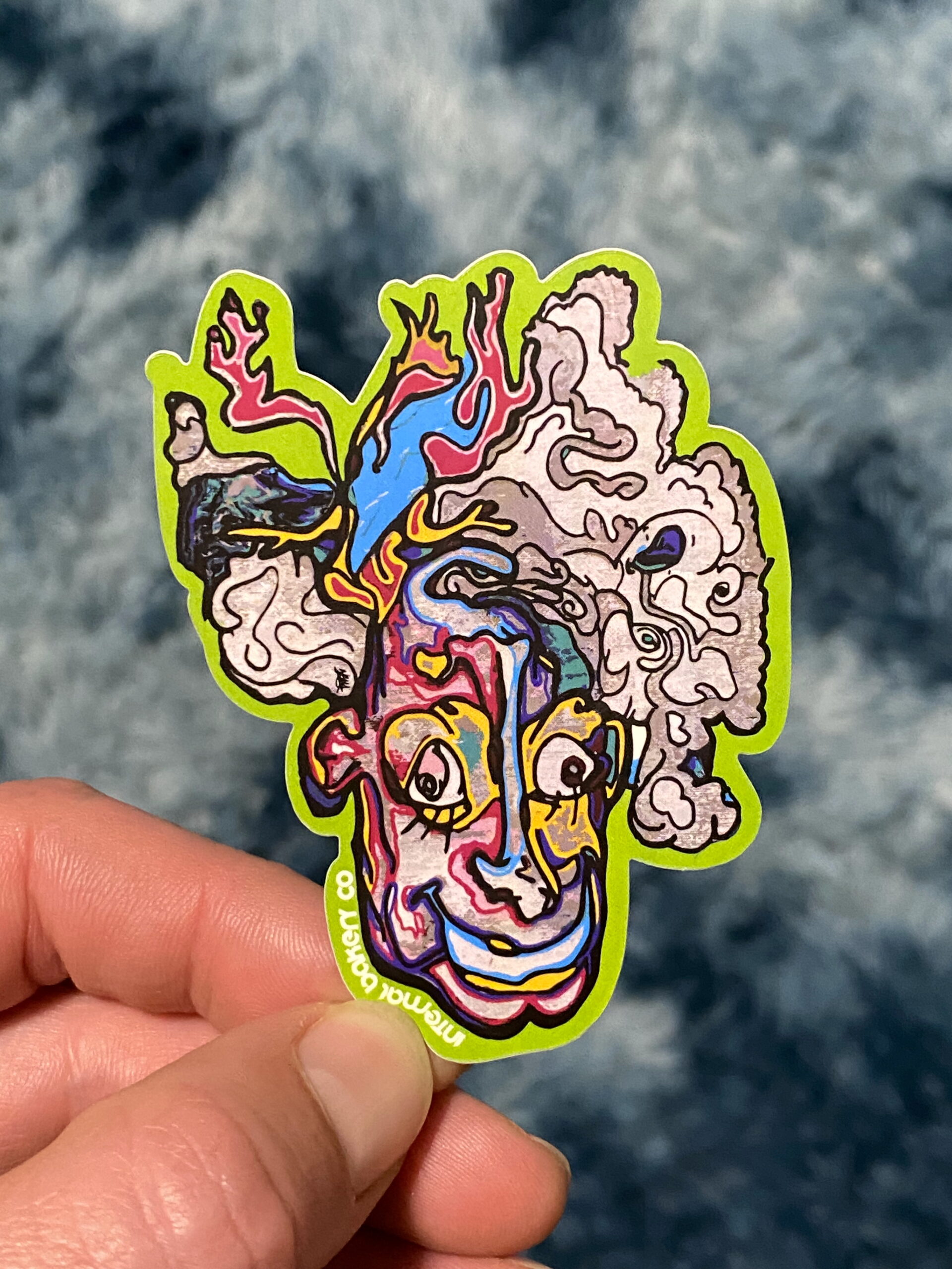 HAZY 2FACE STICKER — 3″ Step into the smoke with Hazy 2Face, a mind-bending character straight from the Internal Bakery imagination. Look at him one way and he’s kickin’ back, blowing out a hazy puff — flip him upside down and suddenly you’re face-to-face with a happy clown from another dimension. Part of the fan-favorite 2Face Series, this hand-drawn design is all about duality, perception, and seeing how imagination can flip the world around you. Perfect for laptops, water bottles, and anywhere you want to remind yourself that there’s always another side to the story. — Hand-drawn by Zach Ray in Colorado Springs, CO — 3″ durable vinyl sticker — Twist it. Flip it. Smoke it out.